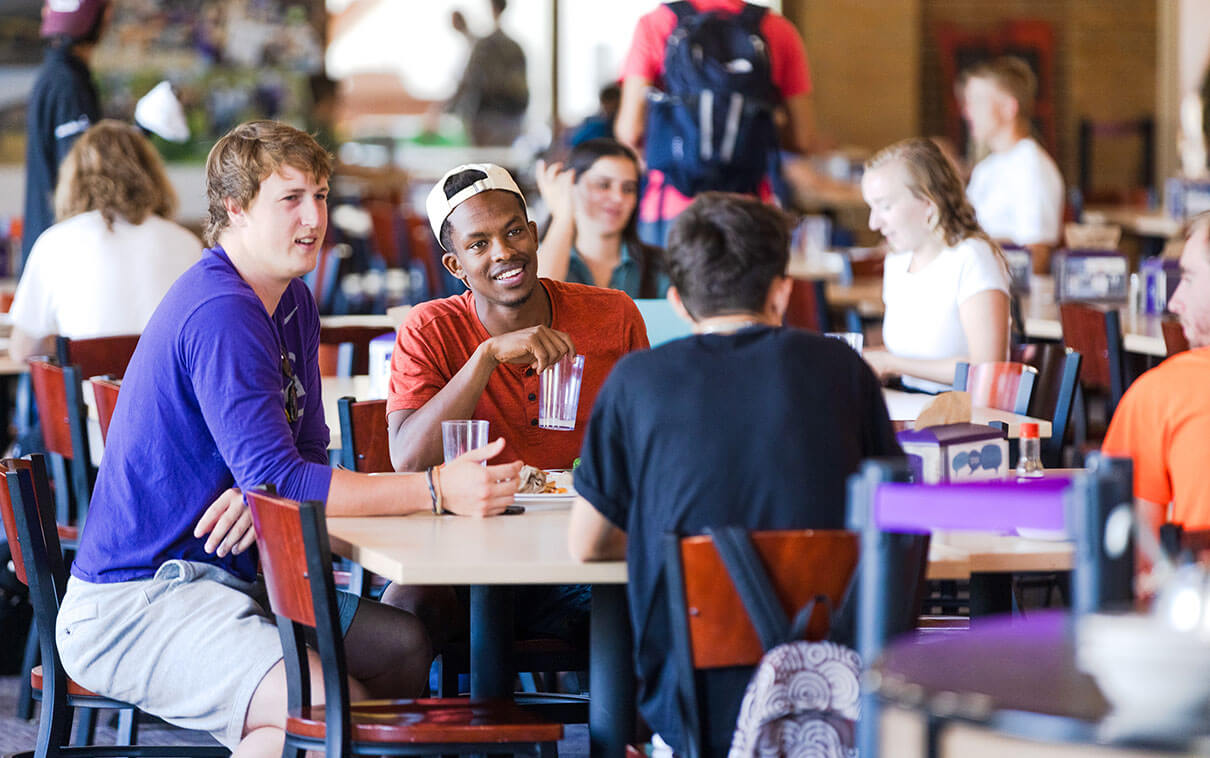 Three students engaged in conversation at the ST. Thomas Aquinas Commons dining hall