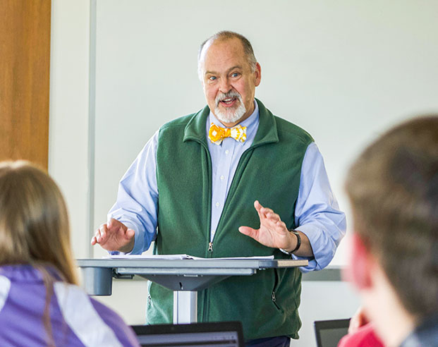 Faculty member in a gray vest and fun yellow bowtie lecturing in front of a small group of students