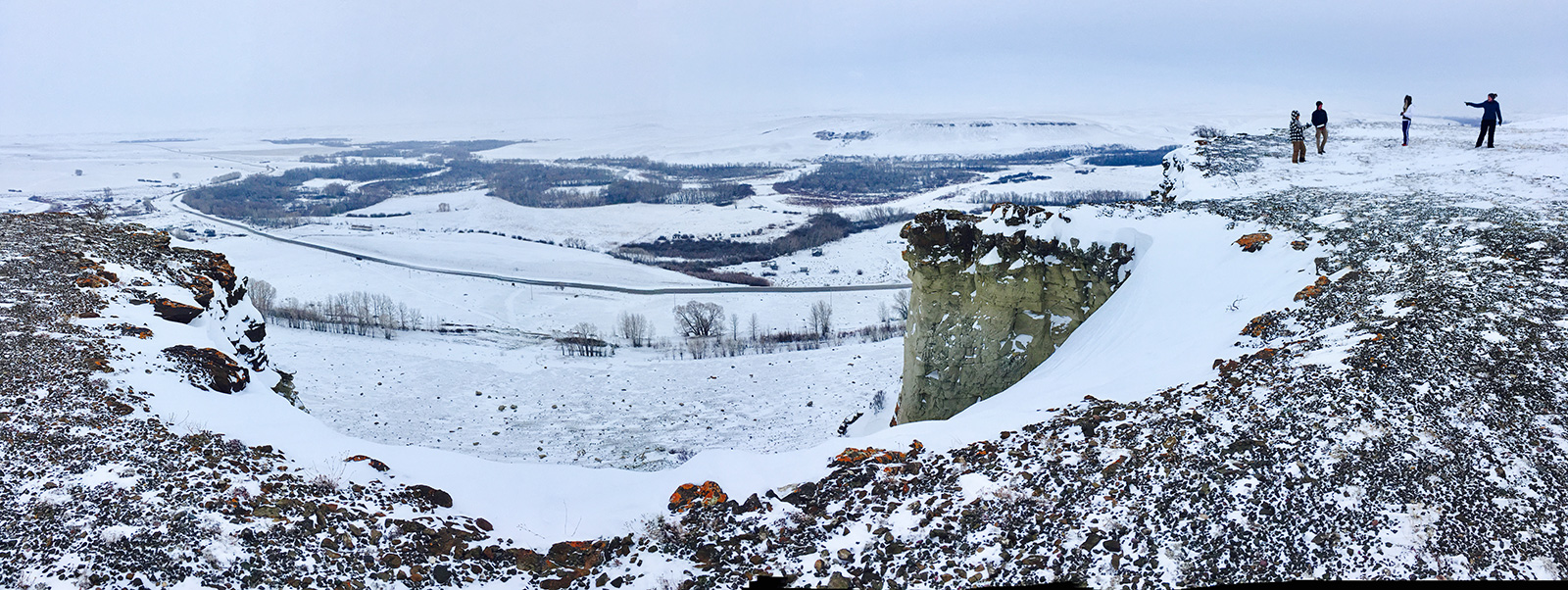 Wintery photograph of small butte and valley with people standing on the butte