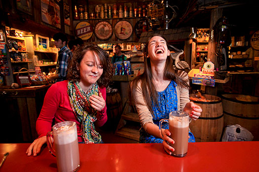 Two students deep in laughter while drinking coffee while one has whipped cream on their nose