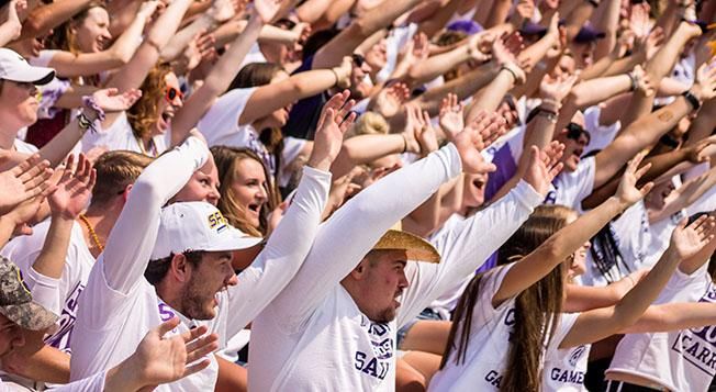 Group of students in the stands an an athletic event all wearing white and moving their hands in sync