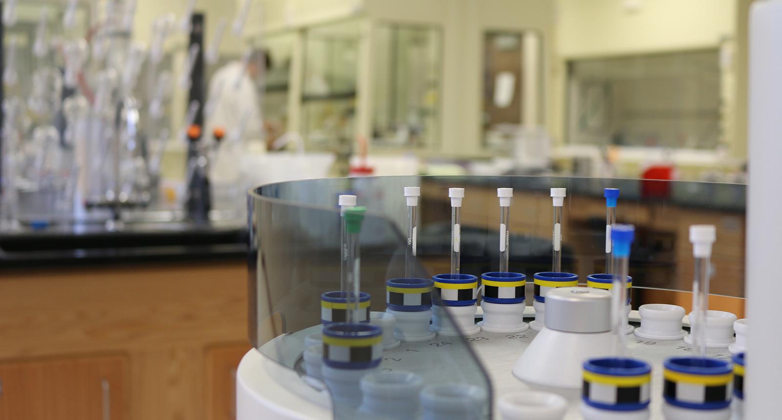 Integrated lab instruments and work tables with a blurred person in a lab coat in the background