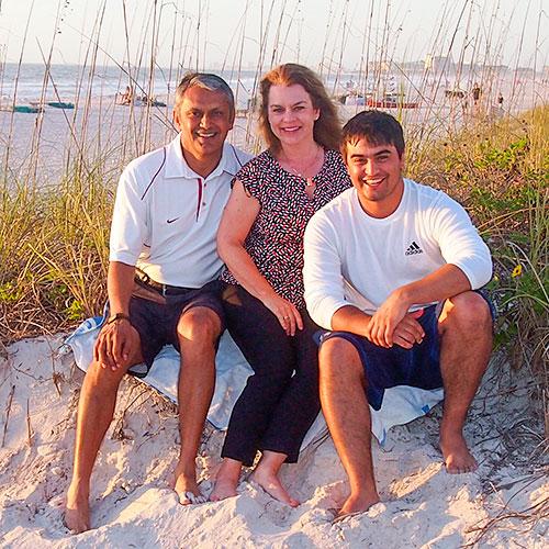 Portrait of Sandy '84 and Raj Lall with son on a sandy beach